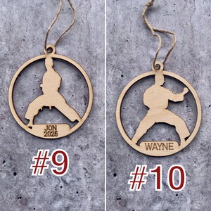 May include: Two wooden ornaments shaped like a karate person with a name and year engraved on each. The ornament on the left says "JON 2025" and the ornament on the right says "WAYNE".
