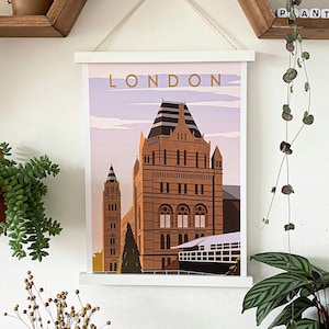 May include: A white framed print with the word "LONDON" in gold lettering. The print features a colorful illustration of a building with a pointed roof and a smaller building in the background.