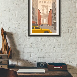 May include: A framed print of a stylized illustration of a yellow taxi cab driving down a street in Brooklyn, New York. The Brooklyn Bridge is visible in the background. The print has the word "BROOKLYN" in the top center.