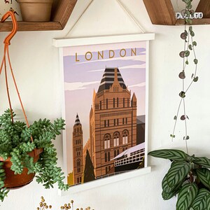 May include: A white framed poster with the word "LONDON" in gold lettering. The poster features a colorful illustration of a building with a pointed roof and a light blue sky.