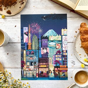 May include: A vibrant print showcasing a stylized Tokyo cityscape at night, with iconic landmarks, fireworks, and traditional buildings. The artwork includes Japanese text and a mountain silhouette. Croissants and coffee cups surround the print.