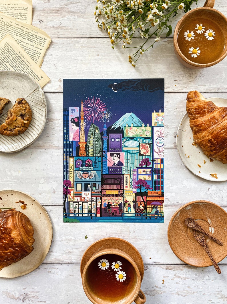 May include: A vibrant illustration of a Japanese cityscape at night, showcasing landmarks such as the Tokyo Tower and Mount Fuji, with fireworks. The image is surrounded by pastries, tea, and flowers, creating a warm, inviting atmosphere.