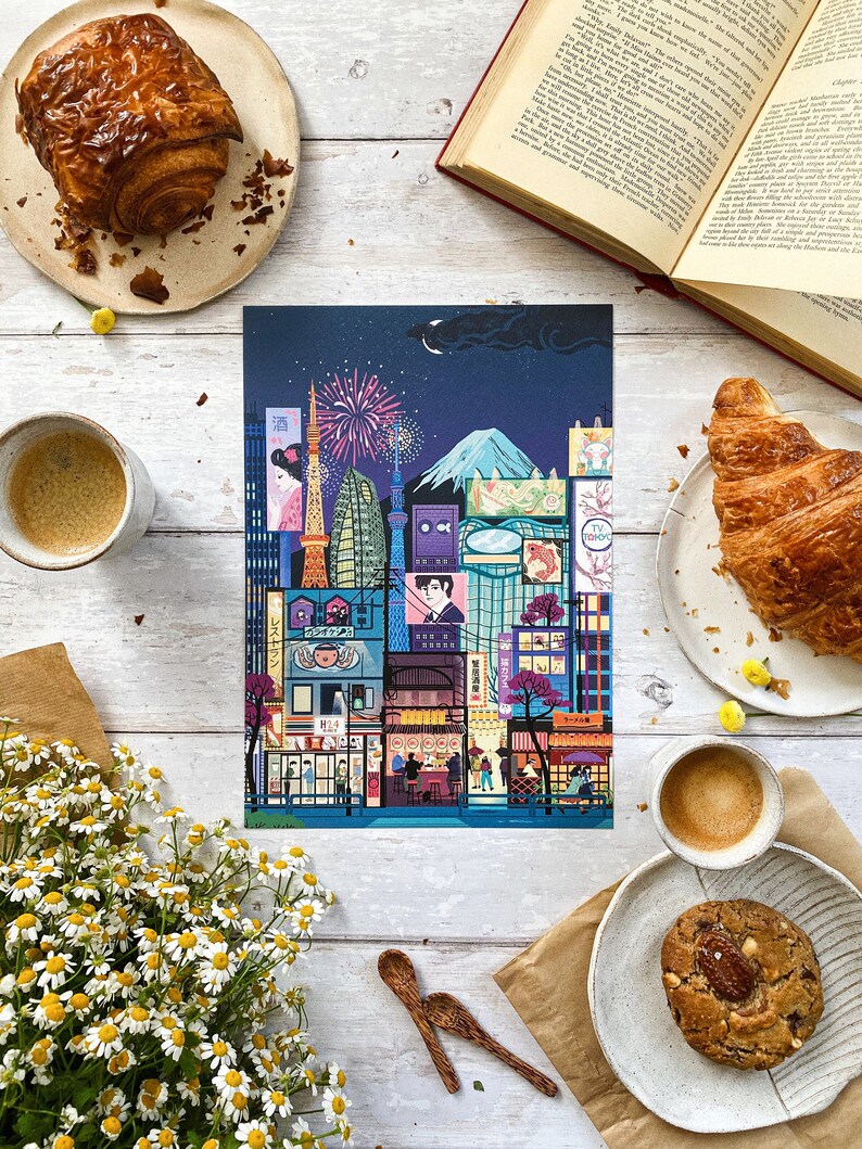 May include: A vibrant print of a Japanese cityscape at night, featuring iconic landmarks, fireworks, and Mount Fuji. The image is complemented by pastries, coffee, a book, flowers, and wooden spoons, creating a warm, inviting atmosphere.