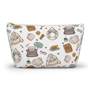 Puede incluir: Un estuche blanco con cremallera que presenta un patrón repetitivo de ilustraciones que incluyen máquinas de escribir, suéteres con diseños de ballenas, salvavidas de Cabot Cove, pilas de libros, tazas de café, gafas, linternas y globos de texto.