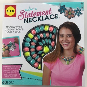 Puede incluir: Un kit de manualidades para hacer collares y pulseras. El kit incluye 60 gemas de plástico de colores en varias formas y tamaños. La caja muestra a una niña usando un collar hecho con las gemas.