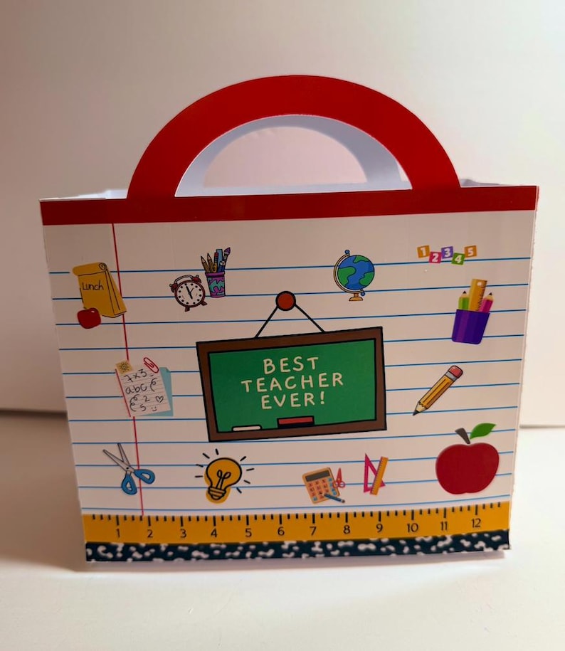 K&ouml;nnte beinhalten: Eine wei&szlig;e Geschenkt&uuml;te mit rotem Griff, verziert mit Aufklebern zum Thema Schule. Die Tasche hat eine gr&uuml;ne Tafel mit der Aufschrift "BEST TEACHER EVER!" und enth&auml;lt Bilder von einem Apfel, einem Bleistift und einem Globus. Der Boden der Tasche hat ein Lineal-Design.
