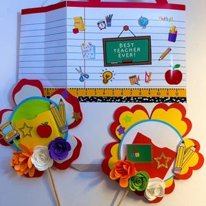 K&ouml;nnte beinhalten: Ein schulthematisches Papierhandwerk mit rotem Griff, das ein liniertes Papierdesign und den Text "BEST TEACHER EVER!" aufweist. Enth&auml;lt Schulmaterial, ein Lineal (ca. 30 cm) und zwei bl&uuml;tenf&ouml;rmige Aufs&auml;tze mit Bleistiften und Papierblumen.