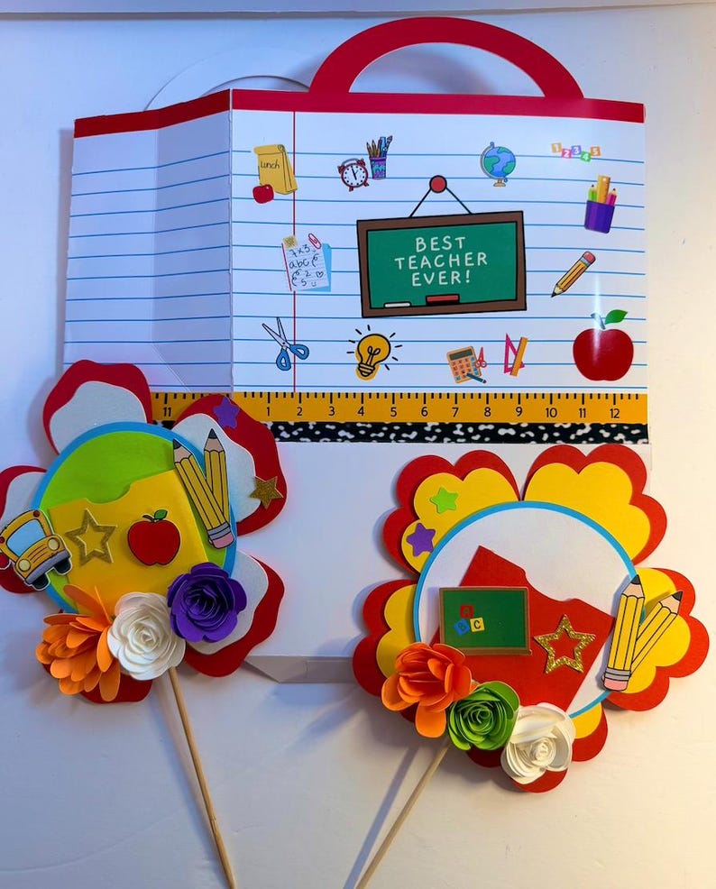 K&ouml;nnte beinhalten: Ein schulthematisches Papierhandwerk mit rotem Griff, das ein liniertes Papierdesign und den Text "BEST TEACHER EVER!" aufweist. Enth&auml;lt Schulmaterial, ein Lineal (ca. 30 cm) und zwei bl&uuml;tenf&ouml;rmige Aufs&auml;tze mit Bleistiften und Papierblumen.