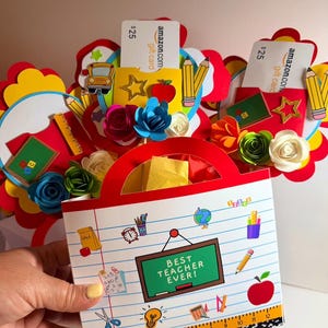 Puede incluir: Una bolsa de regalo hecha a mano para un profesor, con un asa roja y un panel frontal con el texto "Best Teacher Ever!". La bolsa está decorada con recortes temáticos escolares, flores de papel y tarjetas de regalo.