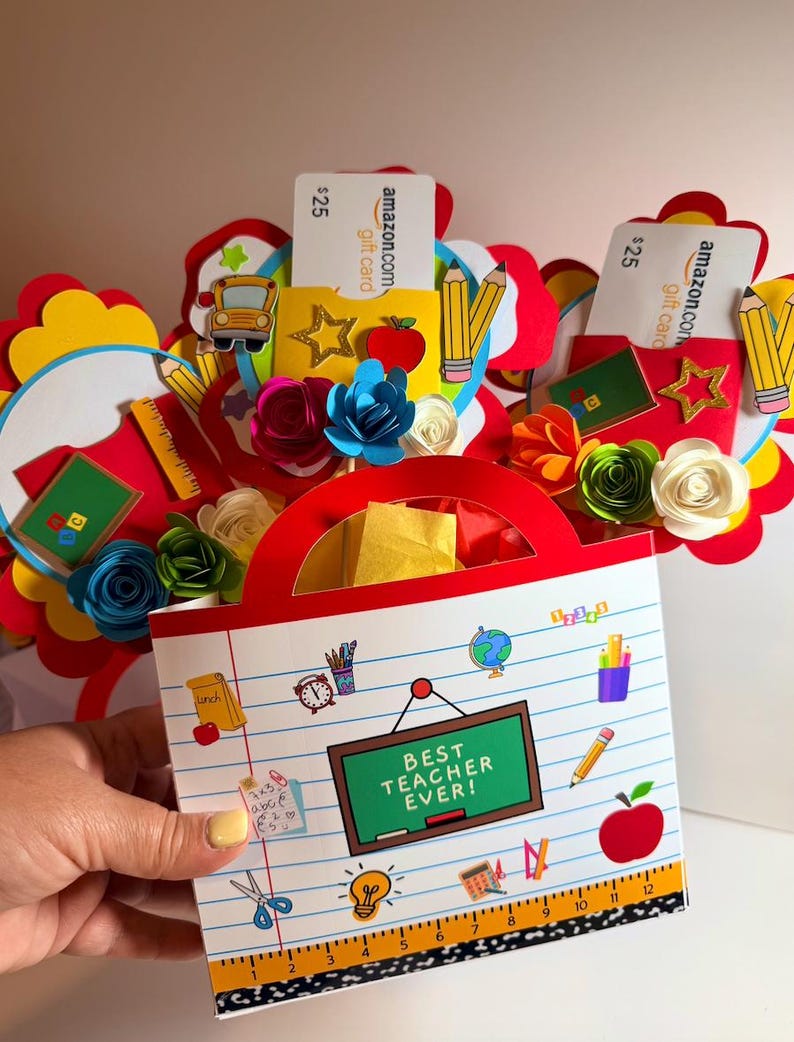 K&ouml;nnte beinhalten: Eine handgefertigte Geschenkt&uuml;te f&uuml;r einen Lehrer, mit einem roten Griff und einer Frontplatte mit dem Text "Best Teacher Ever!". Die Tasche ist mit schulbezogenen Ausschnitten, Papierblumen und Geschenkkarten verziert.