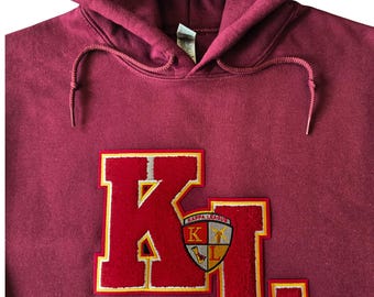 May include: A maroon hooded sweatshirt featuring large, red, felt-like letters K and L on the chest. The letters are outlined in yellow and white. A small shield-shaped patch with the text Kappa League and the letters K and L is centered.