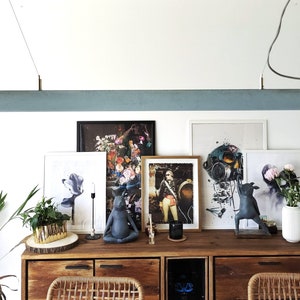 Peut inclure: Un luminaire suspendu rectangulaire bleu clair est suspendu au-dessus d'un buffet en bois. Le buffet présente des œuvres d'art encadrées et des objets décoratifs. Le luminaire porte une inscription dorée et est suspendu par un fin câble.