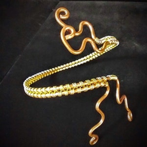 May include: A gold and copper wire bracelet with a unique, twisted design. The bracelet is made of two wires, one gold and one copper, that are twisted together to create a unique and eye-catching design.
