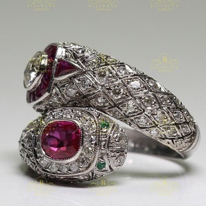 May include: A silver ring with a ruby and diamond snake design. The snake is wrapped around the ring band and has a ruby eye. The ring is set with diamonds and has a detailed design.