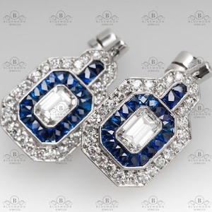 Puede incluir: Un par de pendientes de plata con un diseño geométrico. Los pendientes presentan una piedra central rectangular grande rodeada de piedras de zafiro azul más pequeñas y diamantes transparentes más pequeños.