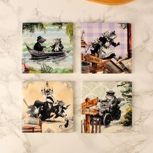 Peut inclure: Ensemble de quatre dessous de verre carrés en céramique avec des illustrations fantaisistes d'animaux anthropomorphes. Les motifs comprennent une scène de bateau, une grenouille en course, un blaireau et une souris, et une grenouille conduisant une voiture.