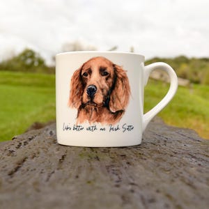 Peut inclure: Une tasse en céramique blanche avec une illustration aquarelle d'un setter irlandais. La tasse porte l'inscription "Life's better with an Irish Setter" imprimée au bas.