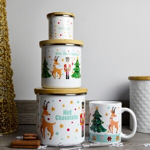 Può includere: Set di quattro barattoli in ceramica bianca con coperchi in legno e motivi natalizi. I barattoli presentano renne, schiaccianoci e alberi di Natale. Il testo sui barattoli recita "Mint Marshmallow", "Sprinkles" e "Hot Chocolate".