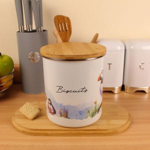 May include: White biscuit jar with a bamboo lid and a silver rim. The jar has a watercolour illustration of puffins and the word "Biscuits". Other white canisters are in the background.