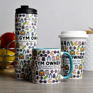 May include: Three white travel mugs with a colourful gym-themed design. The mugs feature a variety of gym equipment icons, including dumbbells, barbells, and yoga mats. The text on the mugs reads "Gym Owner" and "I'm a lot nicer than my resting gym face."