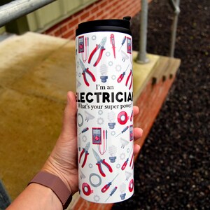 May include: White travel mug with a black lid and a design of electrical tools and the text "I'm an Electrician. What's your superpower?"