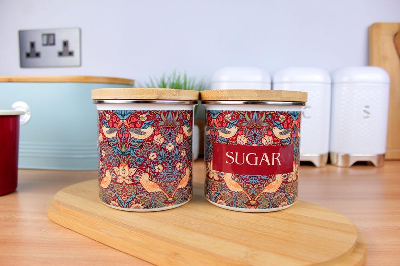 May include: Two ceramic canisters with a floral pattern and a wooden lid. The canister on the right has the word "SUGAR" printed on it.