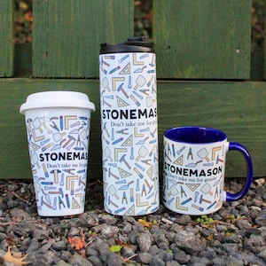 Könnte beinhalten: Drei weiße Keramikbecher mit blauen Akzenten. Die Becher zeigen ein Muster aus Werkzeugen und den Text "STONEMASON Don't take me for granite".