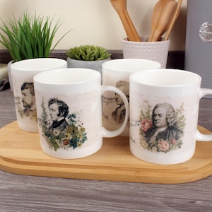 Könnte beinhalten: Vier weiße Keramikbecher mit Porträts von Komponisten, darunter Chopin und Bach, umgeben von floralen Designs. Die Becher stehen auf einem Holztablett vor einem neutralen Hintergrund.
