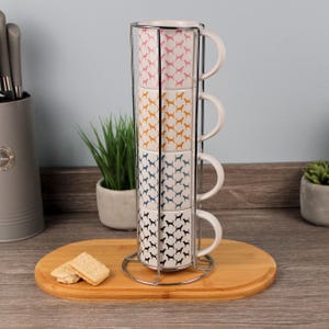 Peut inclure: Un ensemble de quatre tasses en céramique empilées avec un motif de silhouette de chien en rose, orange, bleu et noir. Les tasses sont maintenues dans un support en métal chromé et reposent sur un plateau en bois.