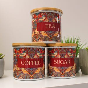 May include: Three ceramic canisters with wooden lids and a floral pattern. The canisters are labeled "Tea", "Coffee", and "Sugar".