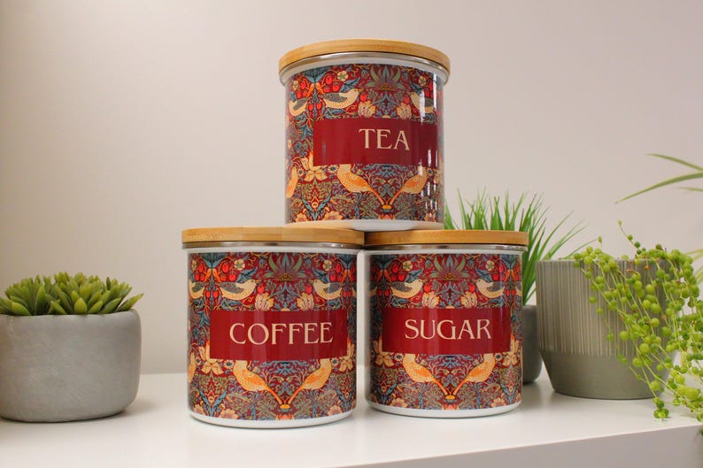 May include: Three ceramic canisters with wooden lids and a floral pattern. The canisters are labeled "Tea", "Coffee", and "Sugar".
