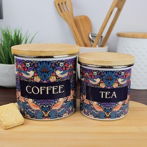 May include: Two ceramic canisters with wooden lids, one labelled "COFFEE" and the other "TEA". Both canisters feature a colourful floral and bird pattern on a dark blue background.