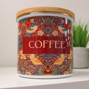 May include: A white ceramic coffee canister with a wood lid. The canister has a red, blue, and green floral pattern with birds and the word "COFFEE" printed on the front.