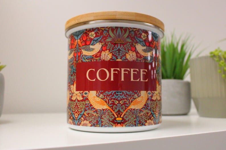 May include: A white ceramic coffee canister with a wood lid. The canister has a red, blue, and green floral pattern with birds and the word "COFFEE" printed on the front.