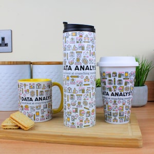 Peut inclure: Trois tasses avec un fond blanc et un motif d'icônes d'analyse de données jaunes et roses. Le texte "DATA ANALYST Excellent at crunching numbers" est sur chaque tasse. Les tasses sont une tasse de voyage haute, une tasse plus courte et une tasse avec un bord jaune.