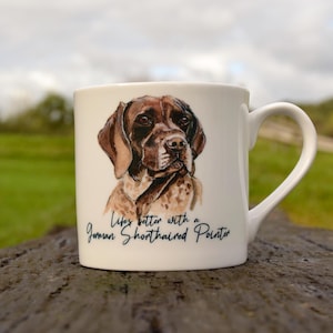 May include: White ceramic mug featuring an illustration of a brown and white German Shorthaired Pointer dog. The mug has the text "Life's better with a German Shorthaired Pointer" printed on it.