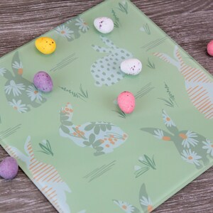 Könnte beinhalten: Ein grünes Glas-Serviertablett mit einem sich wiederholenden Muster aus Hasen und Blumen. Das Tablett ist mit bunten Bonbon-Eiern verziert.