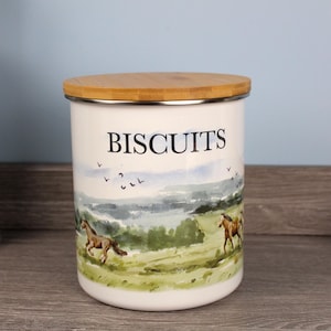 May include: White ceramic biscuit jar with a bamboo lid. The jar features a landscape scene with running horses and the word "BISCUITS" in black lettering. The jar has a silver rim.