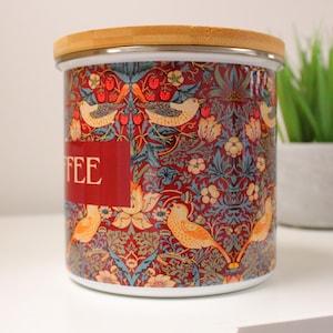 May include: A ceramic coffee canister with a red, blue, and yellow floral pattern and a bamboo lid. The canister has the word "COFFEE" printed on the front.