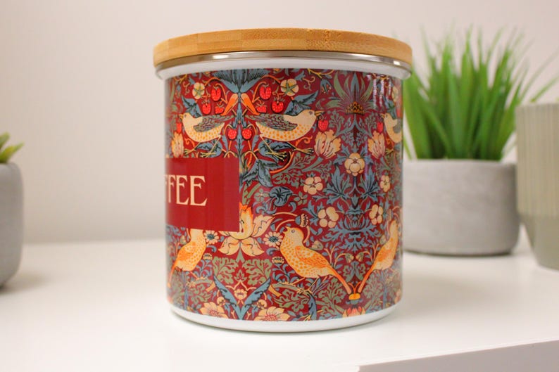 May include: A ceramic coffee canister with a red, blue, and yellow floral pattern and a bamboo lid. The canister has the word "COFFEE" printed on the front.