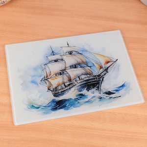 Puede incluir: Una tabla de cortar rectangular de vidrio con una pintura de acuarela de un velero navegando en un mar tormentoso. El barco tiene velas blancas, un casco negro y está rodeado de olas y cielo azules.