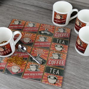 Puede incluir: Un juego de cuatro tazas de cerámica blanca con diferentes diseños de café y té. Las tazas están dispuestas sobre un posavasos rectangular negro y rojo con varios nombres de café y té impresos en él. El posavasos tiene un diseño vintage con un esquema de color rojo y amarillo.