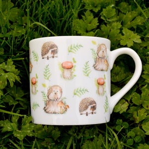 May include: White ceramic mug with a repeating pattern of hedgehogs, mushrooms, and ferns.