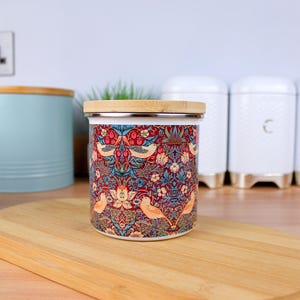 May include: A ceramic canister with a floral and bird design. The canister has a bamboo lid and is sitting on a wooden surface.