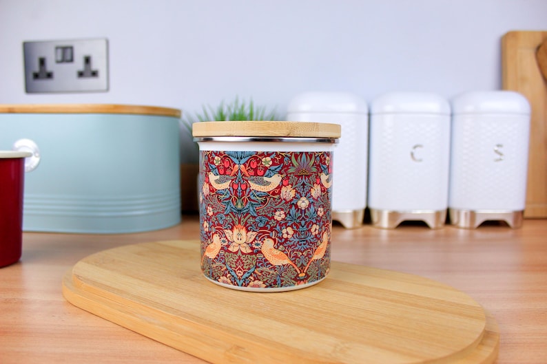 May include: A ceramic canister with a floral and bird design. The canister has a bamboo lid and is sitting on a wooden surface.