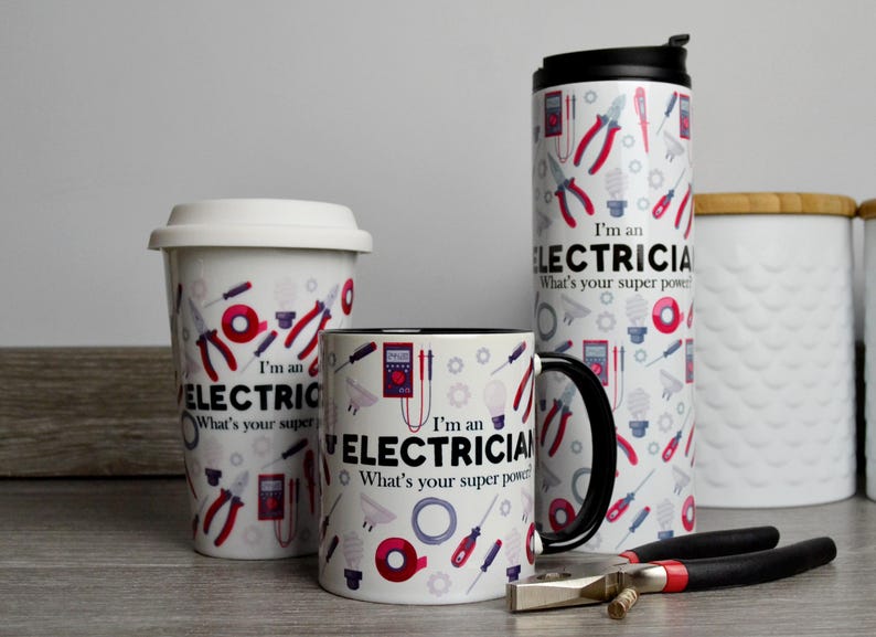 May include: Three mugs with a white background and black handles. The mugs have a pattern of electrical tools and the text "I'm an Electrician. What's your super power?"  The mugs are on a gray surface with a pair of pliers.
