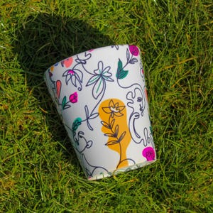Puede incluir: Taza reutilizable blanca con un diseño floral y abstracto colorido. El diseño presenta colores rosa, amarillo, verde y azul.