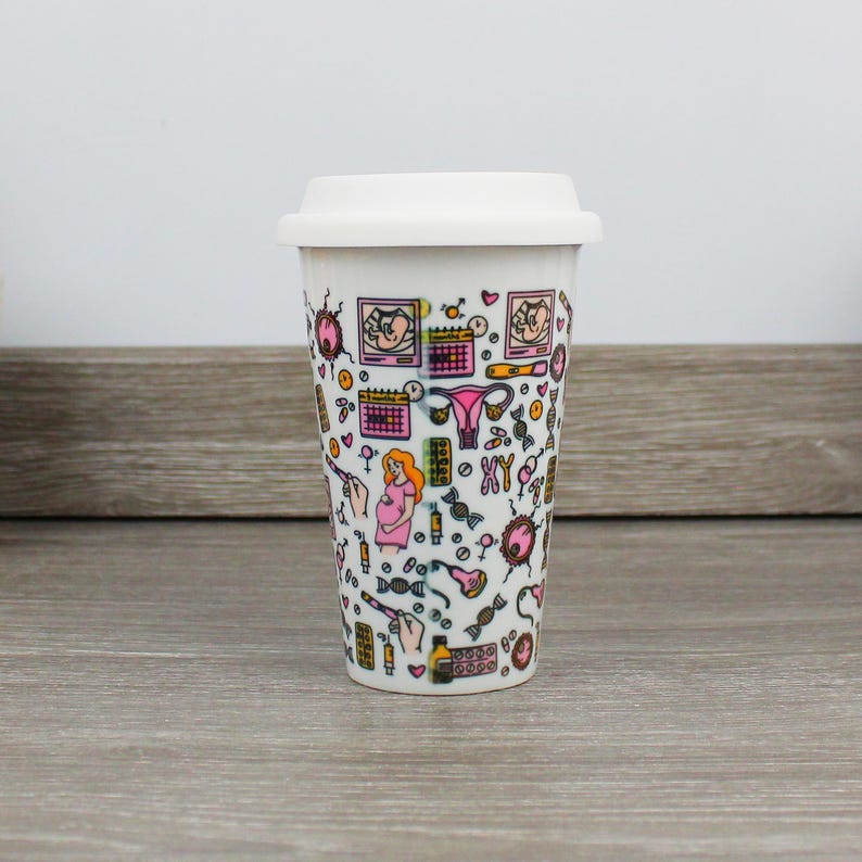 May include: White travel mug with a pink and black design featuring illustrations of pregnancy, fertility, and motherhood. The design includes images of a uterus, a calendar, a baby, and a DNA strand.
