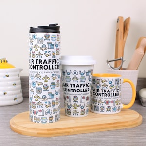 Könnte beinhalten: Ein Set von Trinkgefäßen zum Thema Luftfahrt. Es umfasst einen Reisebecher, einen Becher und eine Tasse. Die Artikel sind weiß und weisen ein sich wiederholendes Muster aus Flugzeugen und Tower-Symbolen auf. Der Text "AIR TRAFFIC CONTROLLER" ist aufgedruckt.