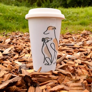 Könnte beinhalten: Weiße Keramik-Reisebecher mit einer schwarzen Linienzeichnung von zwei Windhunden. Der Becher hat einen schwarzen Deckel.